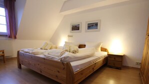 Een houten bed in een kamer met een schuine kap, een nachtkastje en een bijzettafeltje.
