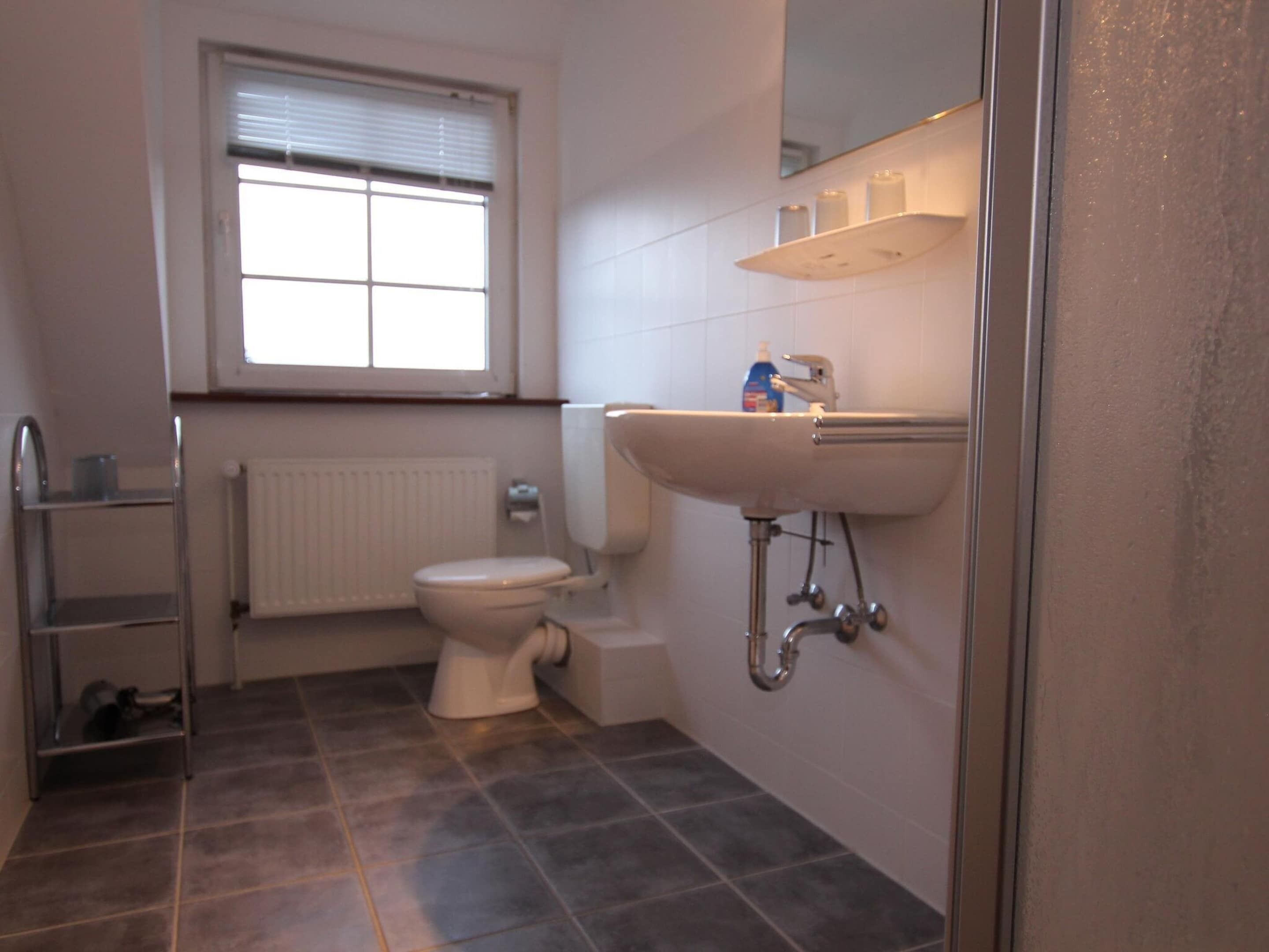 A bathroom with a toilet, a sink, a window, and a radiator.
