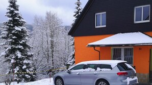 A house with a car parked in front, surrounded by snow-covered trees. - Ferienhaus, Oberwiesenthal (Oberwiesenthal)