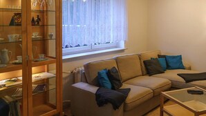 A living room with a beige sofa, a glass coffee table, and a bookshelf filled with books and decorative items. - Ferienhaus, Oberwiesenthal (Oberwiesenthal)