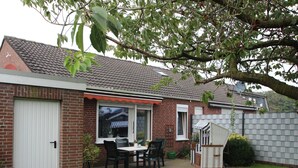 Une maison en briques avec un toit en tuiles, une porte blanche et une terrasse avec une table et des chaises.