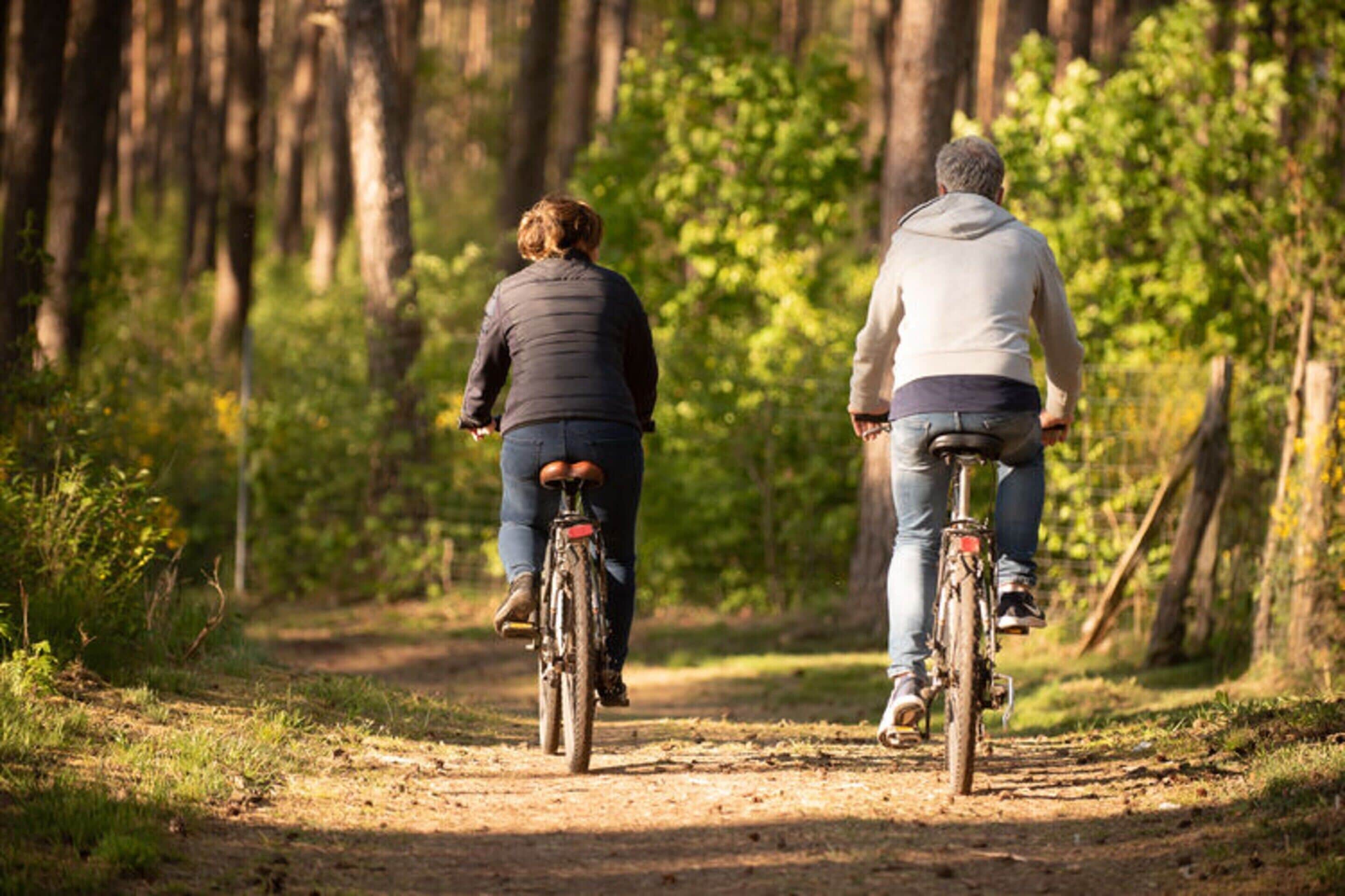 Dos personas andando en bicicleta por un sendero de tierra rodeado de árboles.