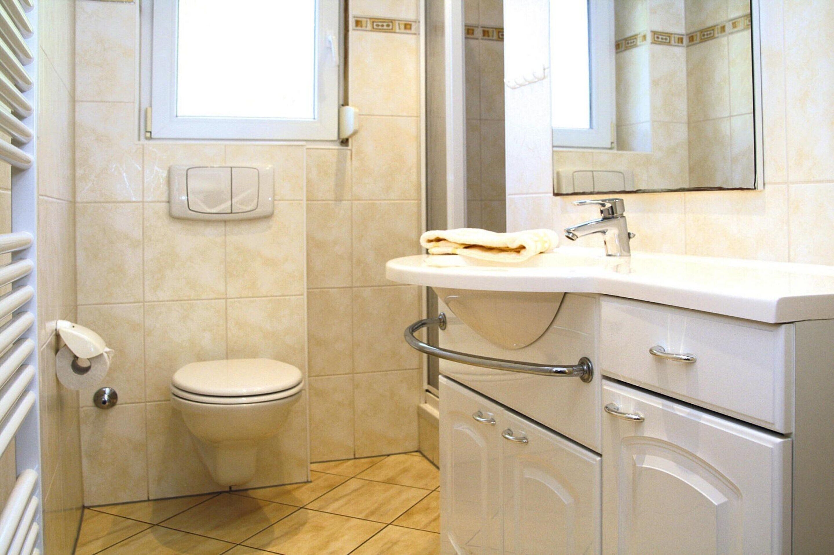 A bathroom with a toilet, sink, mirror, and storage cabinets.