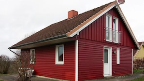 A red two-story house with a gabled roof, a small balcony on the second floor, and a satellite dish on the roof. - Ferienhaus am Moenchneversdorfer See, Moenchneversdorf (Schoenwalde am Bungsberg)