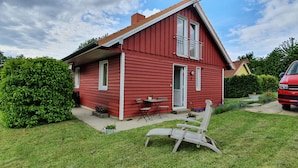 A red house with a small patio, a chair, and a car parked nearby. - Ferienhaus am Moenchneversdorfer See, Moenchneversdorf (Schoenwalde am Bungsberg)