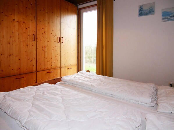 A room with two beds, wooden wardrobe, and a window with curtains. - Ferienhaus am Moenchneversdorfer See, Moenchneversdorf (Schoenwalde am Bungsberg)
