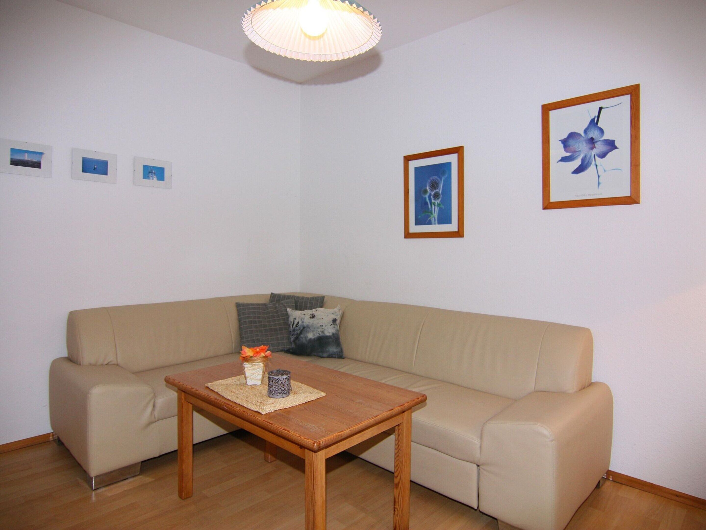 A living room with a beige sofa, a wooden coffee table, and three framed pictures on the wall.