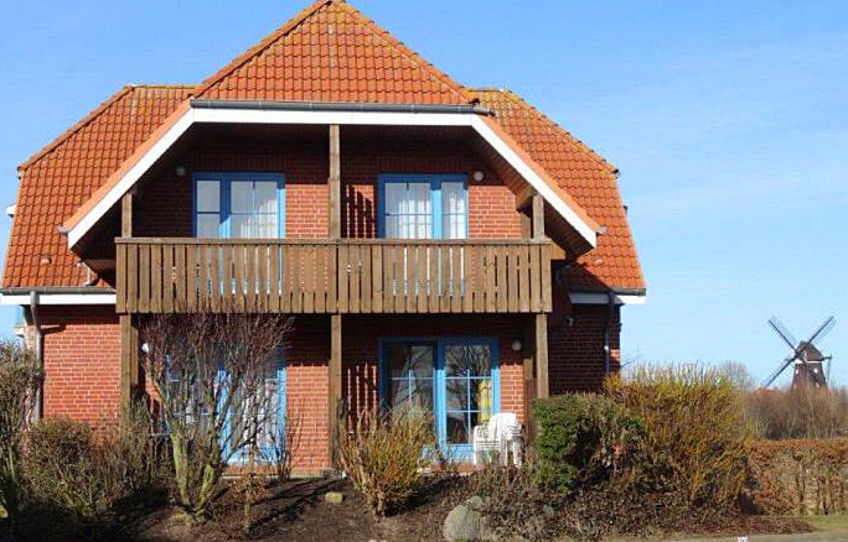 A two-story house with a red-tiled roof, a wooden balcony, and a windmill in the background.