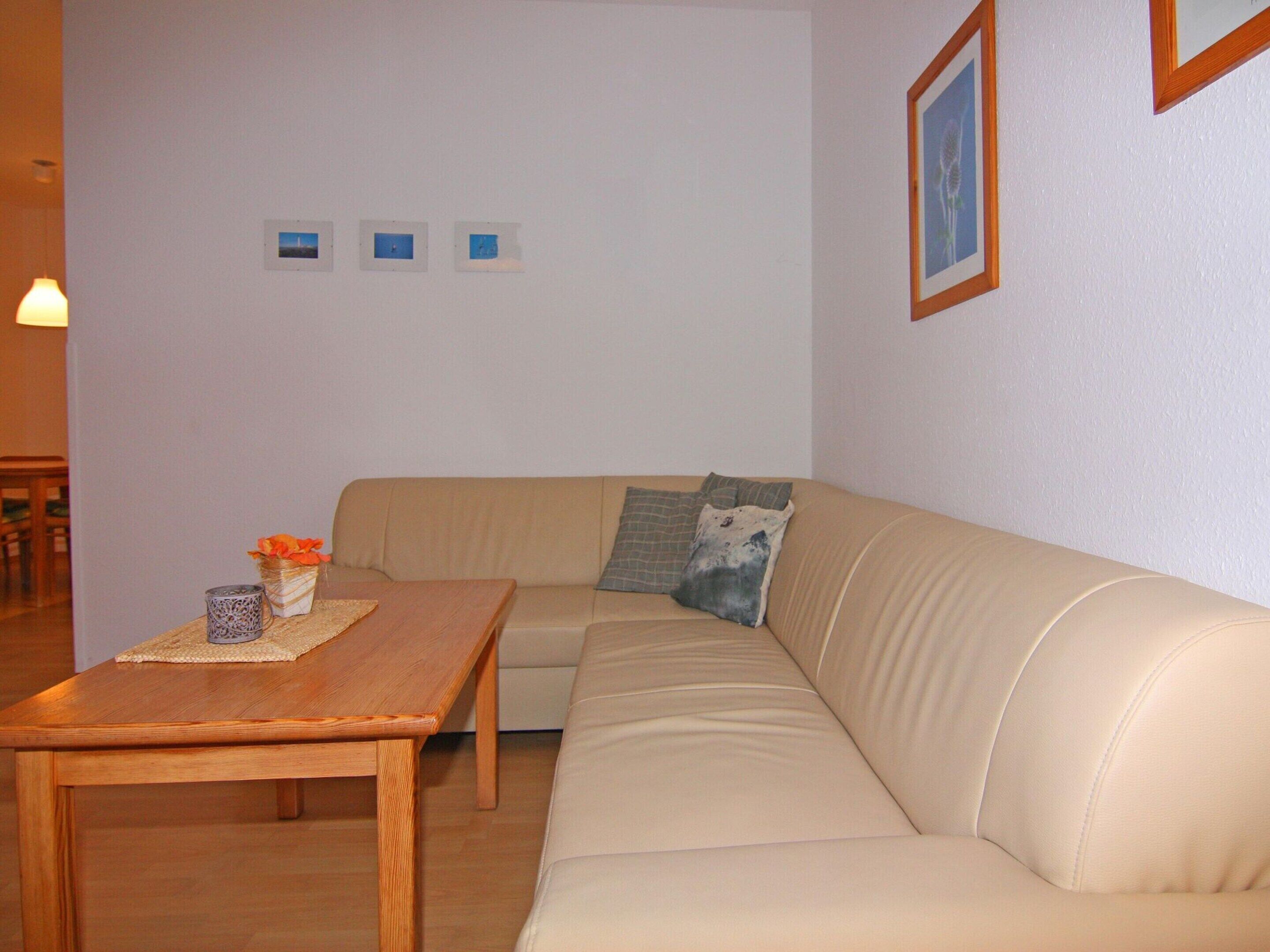 Ein Wohnzimmer mit einem beigen Sofa, einem Holztisch und drei gerahmten Bildern an der Wand.