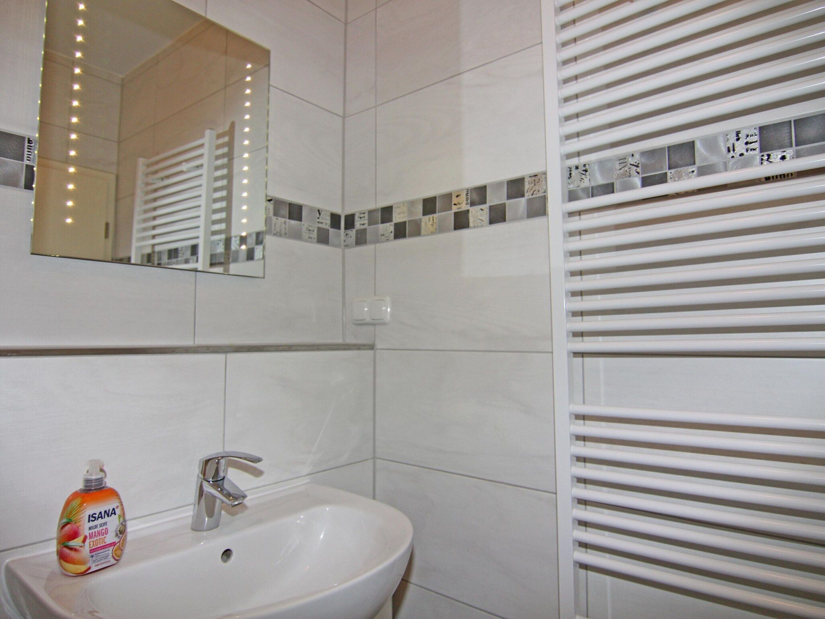 Une salle de bain avec un lavabo blanc, un miroir et un flacon de savon pour les mains parfumé à la mangue exotique de la marque Isana.