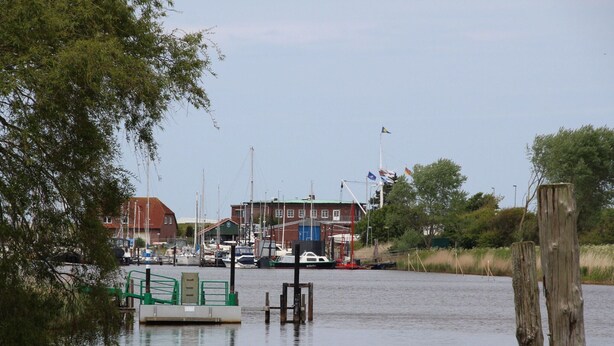 En småbåtshamn med förtöjda båtar, en byggnad med ett rött tak och en flaggstång med flaggor.
