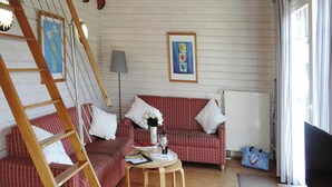 Ett mysigt rum med en trästege, en röd- och vitrutig soffa, ett litet runt bord med en flaska och glas, och en tv-apparat på ett träställ.
