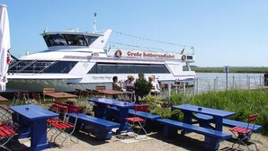 En båt med sittplatser och bord utomhus, en livboj och en skylt med texten ”Große Boddenfahrt”.