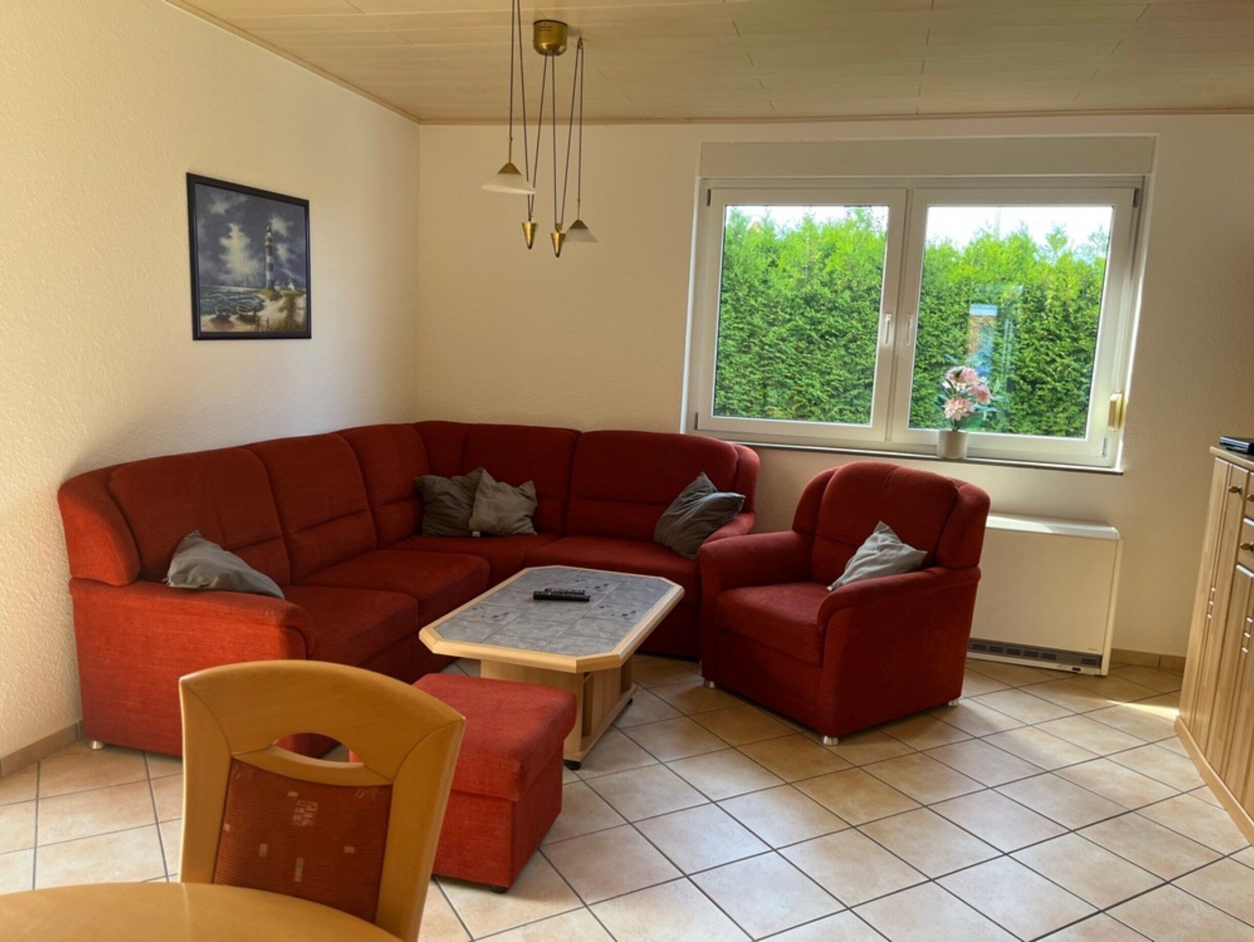 A cozy living room with a red sectional sofa, a wooden coffee table, and a yellow chair. There is a window with a view of greenery outside.