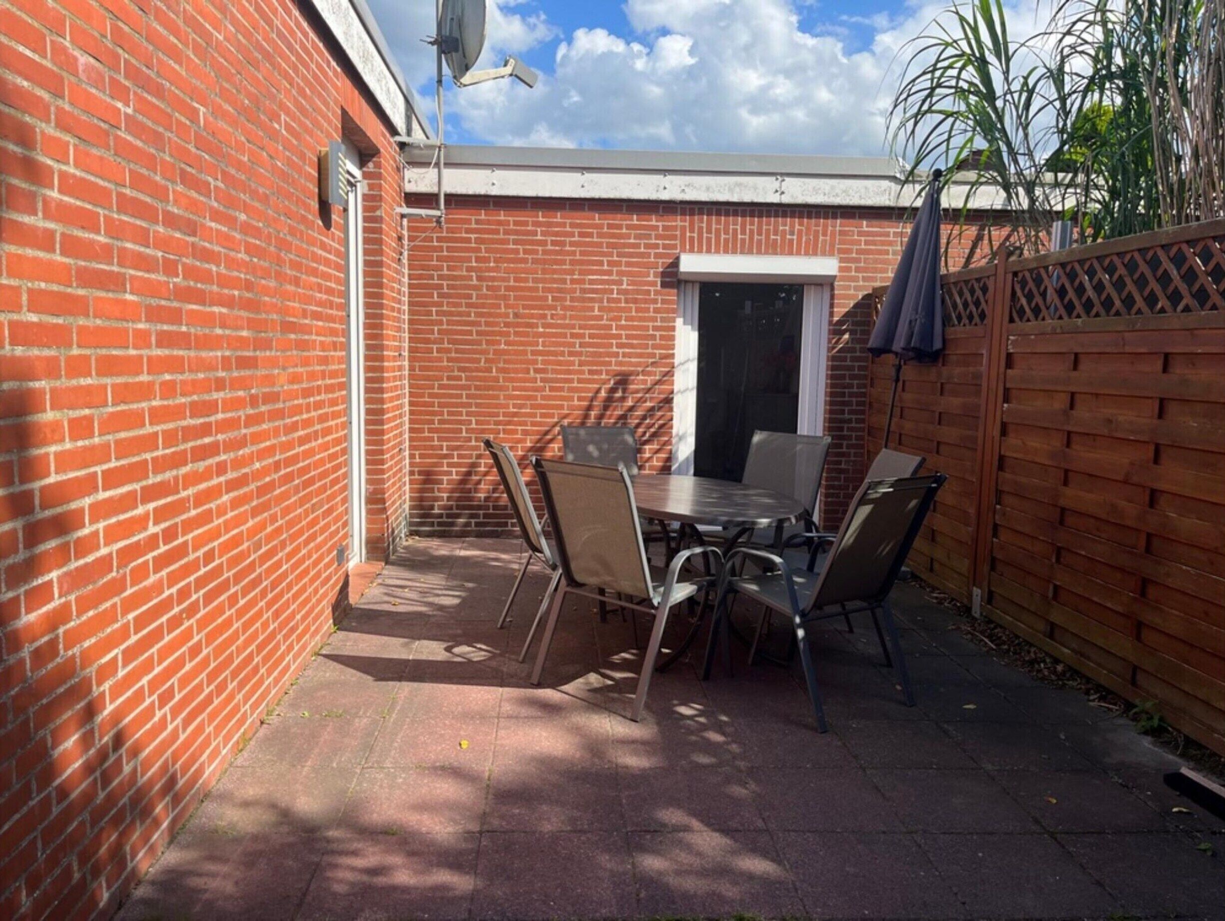 A patio with a brick wall, a table with chairs, and a wooden fence.