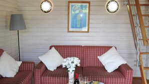 A cozy room with a red patterned sofa set, a small round table with a bottle and glasses, and two wall-mounted lights. - Ferienhaus in Lissendorf bei Eifel Wegen (Lissendorf)