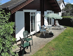 Eine Terrasse mit Sitzgelegenheiten im Freien, einem grünen Sonnenschirm und einem weißen Gebäude mit einer Schiebetür.