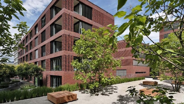 A modern building with a brick facade, multiple windows, and a courtyard with seating and greenery. - Ferienhaus in Lissendorf bei Eifel Wegen (Lissendorf)