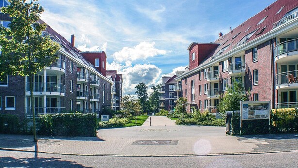 Une rue résidentielle bordée d’immeubles d’appartements en briques, avec une allée piétonne centrale et des espaces verts.