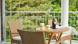 Un balcon agrémenté de meubles en osier, une table ronde en bois, des bougies, une bouteille de vin et un verre de vin rouge.