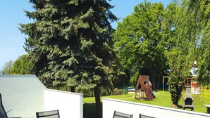 A patio area with a table and chairs, a wooden play structure, and a large tree. - Wohnung mit Terrasse in Sommersdorf (Sommersdorf)