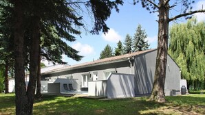 A modern building with a flat roof, large windows, and a covered outdoor seating area with two chairs. - Wohnung mit Terrasse in Sommersdorf (Sommersdorf)