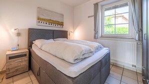 Une chambre à coucher avec un lit, une table de chevet, une lampe et une fenêtre avec des rideaux.