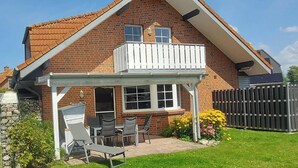 Une maison à deux étages, construite en briques, dotée d’un balcon, d’une terrasse couverte avec des meubles d’extérieur et d’une clôture en pierre.