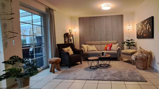 Un salon comprenant un canapé, des fauteuils, une table basse et une grande fenêtre avec des rideaux.