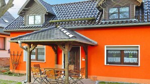 Ett tvåvåningshus med ett tak täckt av tegelpannor, en täckt uteplats med trämöbler och en ljusorange fasad.