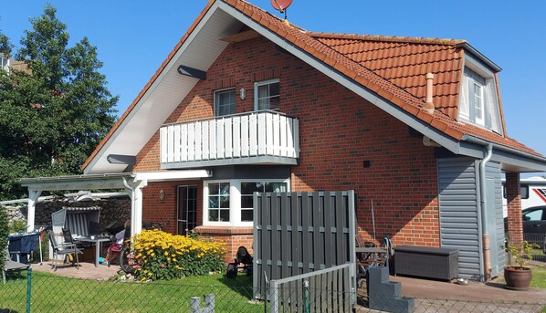 Une maison à deux étages, construite en briques, avec un toit en pente, un balcon et une cour clôturée.