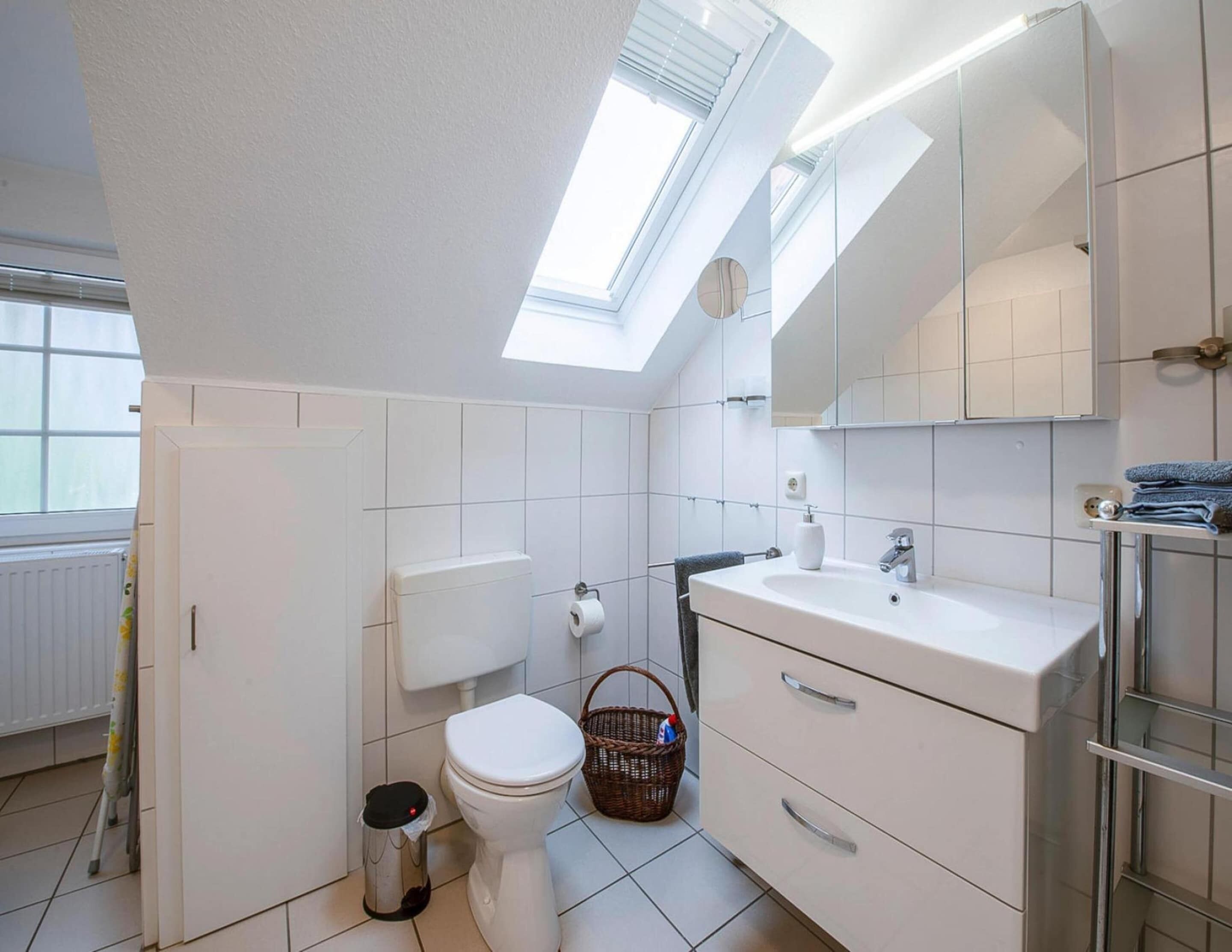 Un bagno moderno con un lucernario, piastrelle bianche, un WC, un lavandino e uno specchio.