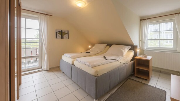 A bedroom with a bed, a nightstand, a window, and a view of the outside. - Ferienwohnung im OG in Friedrichkoog-spitze (Friedrichskoog)