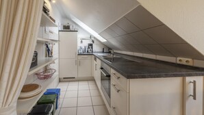 A compact kitchen with white cabinets, a black countertop, and a built-in oven. - Ferienwohnung im OG in Friedrichkoog-spitze (Friedrichskoog)
