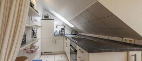 Een kleine keuken met witte kastjes, een zwart aanrecht en een ingebouwde oven.