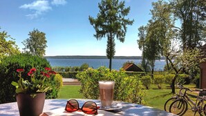 An open book, a pair of sunglasses, and a glass of beverage on a table with a view of a lake and greenery. - Seepark Heidenholz, Plau am See (Plau am See)