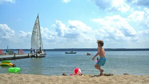 A beach with a sailboat, inflatable rings, and a sandy shore. - Seepark Heidenholz, Plau am See (Plau am See)