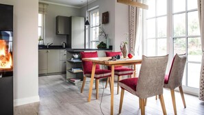 Eine moderne Küche mit Essbereich, ausgestattet mit einem Holztisch, roten Stühlen, einem Kamin und großen Fenstern.