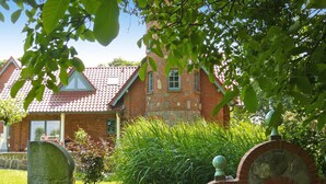 A brick house with a red-tiled roof, surrounded by greenery and a stone monument. - Ferienhaus, Plau am See (Plau am See)