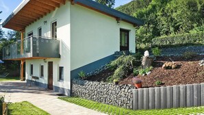 Una casa moderna de dos pisos con balcón, pared de piedra y jardín con plantas y una estatua.