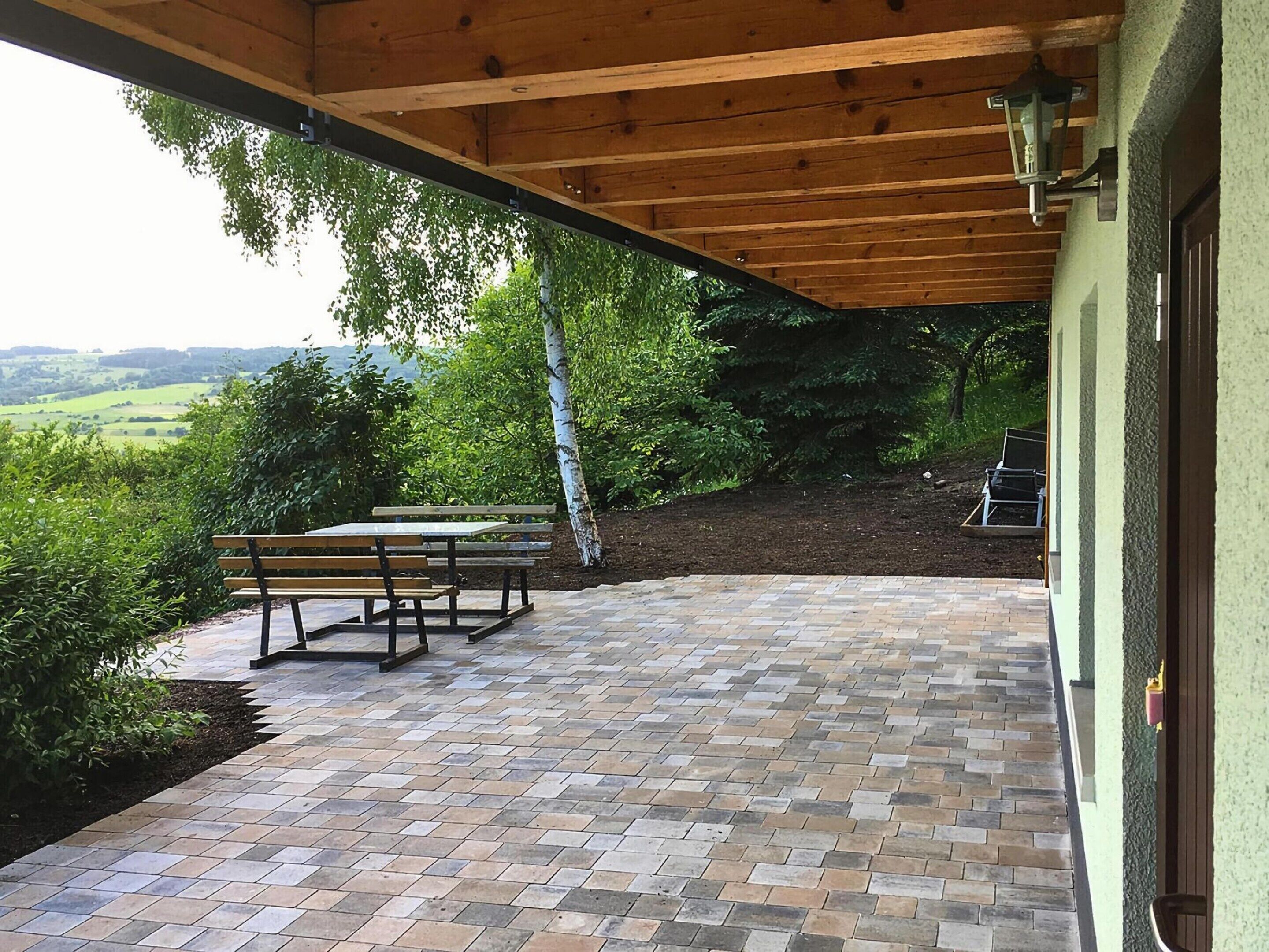 Eine Terrasse im Freien mit einer Holz-Pergola, einem Picknicktisch und Blick auf eine grüne Landschaft.
