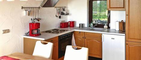 Cocina compacta con armarios de madera, lavavajillas, estufa y pileta. Hay utensilios colgando y una cafetera roja sobre la encimera.