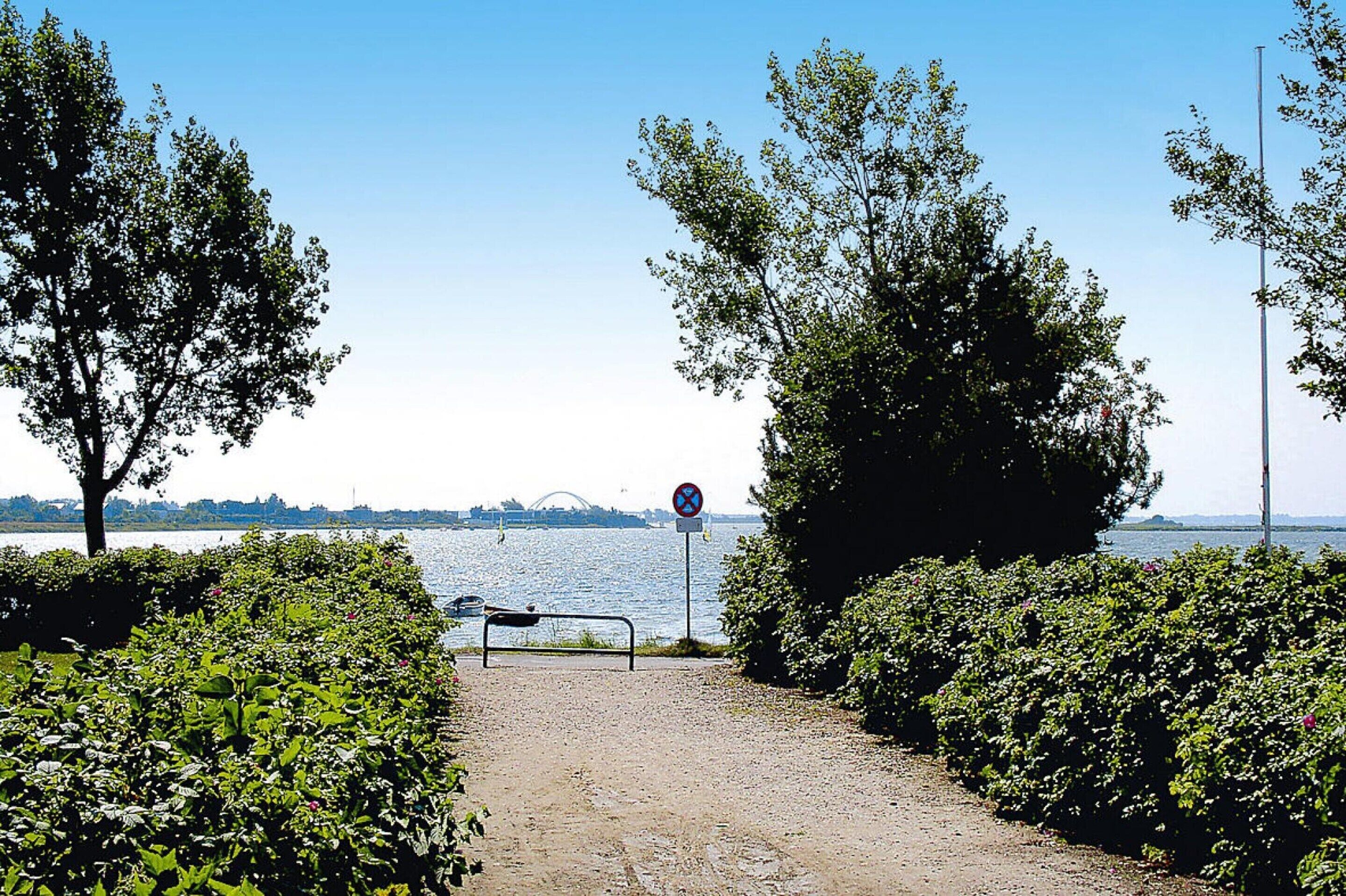 A pathway leading to a body of water with a no-entry sign, surrounded by greenery and trees.