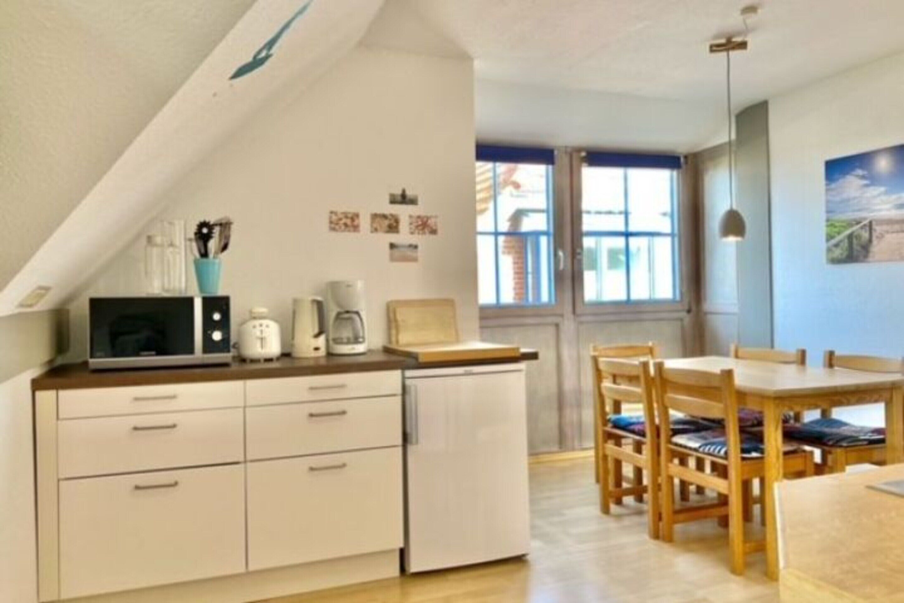 Ett kompakt kök med vita skåp, en mikrovågsugn, en kaffebryggare och en matplats med trästolar och ett bord.
