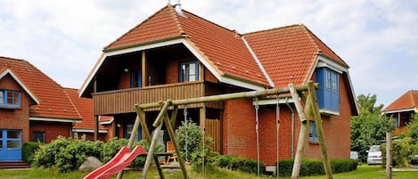 Ein Wohnhaus mit rotem Ziegeldach, einer hölzernen Schaukel und einer roten Rutsche im Garten.