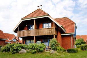 Ein zweistöckiges Haus mit Holzbalkon, Backsteinfassade und rotem Ziegeldach.