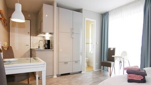Moderni hotellihuone, jossa on pieni keittiö, ruokailutila ja sänky.