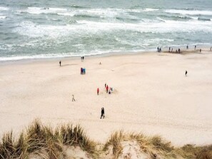 A beach with people walking and playing, and some dunes in the foreground. - 4 Star Holiday Home in Ulfborg (Ulfborg)