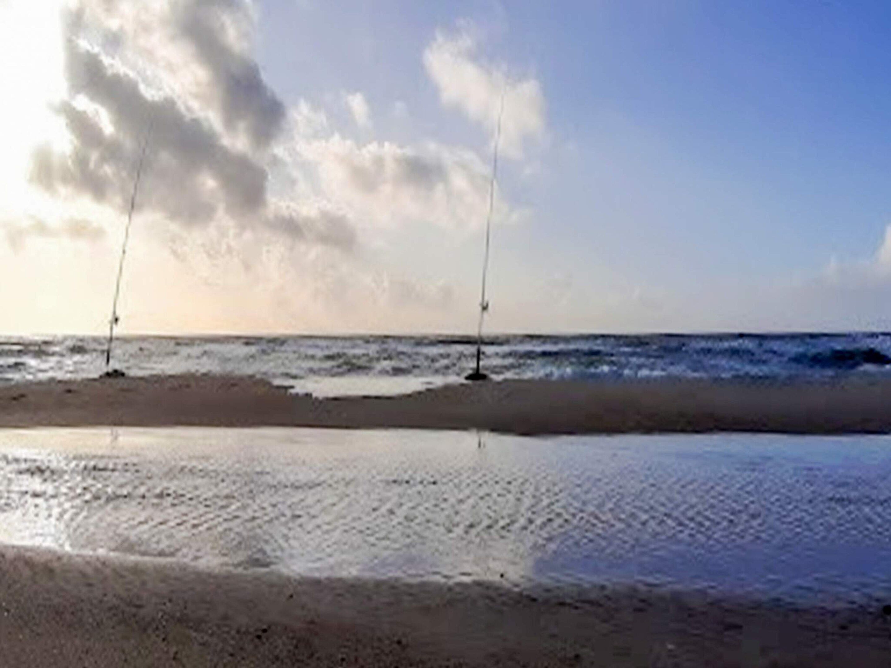 A beach with two poles and a calm sea.