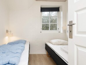 A small, single-room accommodation with a bed, a bedside table, a lamp, and a window with a view of trees. - 4 Star Holiday Home in Ulfborg (Ulfborg)